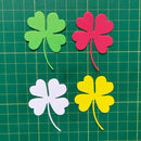 Four colorful paper shamrocks on a green grid background
