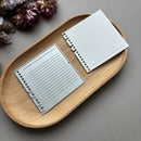 Two metallic notepads on a wooden tray with a gray background