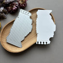 Two metal bookmarks shaped like the state of Illinois on a wooden tray with dried flowers.