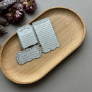 Metal die cutters shaped like notebooks and labels on a wooden tray with flowers in the background.