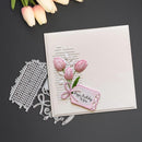Card with pink tulips and 'Happy Birthday' tag, accompanied by a metal cutting die on a dark background.