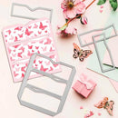 Butterfly-themed crafting items on a pink surface with flowers and a gift box.