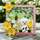 Card with a cute cartoon lamb design, flowers, and a pink border on a wooden surface.