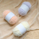 Three skeins of yarn in peach, white, and cream on a beige fabric background