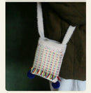 Small bag with colorful pattern and pom-poms attached to a dark coat.