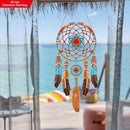 Decorative dreamcatcher with feathers hanging by a window with a view of the ocean.
