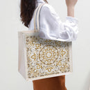 Person holding a tote bag with a gold mandala design on a plain background