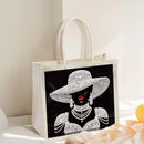 White tote bag with a decorative design of a woman wearing a hat and jewelry on a light background.