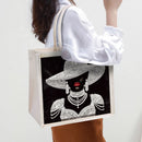 Tote bag with a design of a woman wearing jewelry on a black background, held by a person.