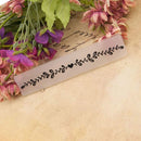 Decorative metal bookmark with floral design on a textured surface with flowers.