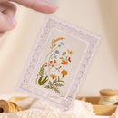 Hand-embroidered floral design on a lace doily held by a hand against a neutral background.