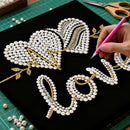 Handmade jewelry design with pearls and gold elements on a black background, with a hand holding a pink pen.