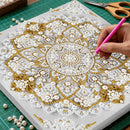 Mandala art with beads and a hand using a pink tool on a green cutting mat.