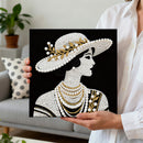 Person holding a decorative painting of a woman wearing a pearl-studded hat and jewelry.