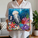Person holding a completed diamond painting of an underwater scene with jellyfish, starfish, and coral.