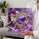 Person holding a diamond painting with a heart design and nature scene, set against a purple background.