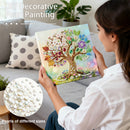 Woman holding a DIY decorative pearl painting of a tree with colorful flowers, sitting on a couch.