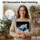 Woman holding a decorative painting of a turtle with pearls and sequins on a table.