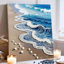 Canvas painting of a beach scene with waves and pearls, placed on a surface with candles and decorative items.
