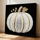 Decorative pumpkin art piece made of pearls and gold beads on a black background