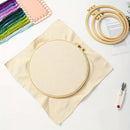 Embroidery hoop with fabric on a white surface, surrounded by colorful threads and tools.