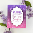 Card with 'We love, because He first loved us' text on a purple and pink floral background