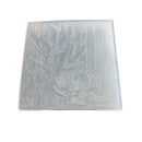 A square translucent plastic craft stamp or embosser with a floral magnolia design and wood grain texture, shown on a plain white background.