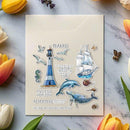 Card with lighthouse, sailboat, and dolphins design on a marble surface with flowers.