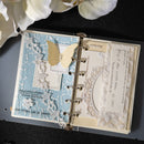 Open scrapbook with decorative pages and a butterfly on a dark surface with white flowers.