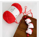 Red yarn ball with a white label next to a small crocheted cat toy on a wooden surface.