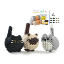 Three crocheted cat toys in black, beige, and gray with yarn and hooks on a white background.