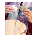 Close-up of hands holding a small white object and a beige knitted item against a textured fabric background.