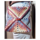 Colorful crocheted bag held by a person wearing jeans.