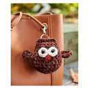 Brown owl-shaped keychain attached to a brown leather bag with a blurred natural background.