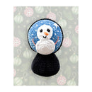 Crocheted snowman amigurumi with a blue top and black base on a festive background.