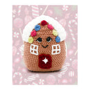 Crocheted gingerbread house toy with a pink background featuring candy cane and star patterns.