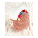 Crocheted amigurumi resembling a gingerbread house with colourful pom-poms on a soft white background