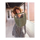 Woman holding a green woven bag in an outdoor setting