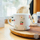 White mug with cherry and flower design on a wooden surface