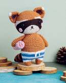 Crocheted raccoon toy on a wooden stand with a light green background