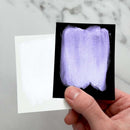 Hand holding a small black card with a purple paint swatch against a marble background