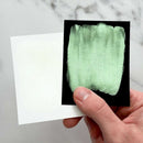 Hand holding a swatch of green fabric against a white card on a marble surface