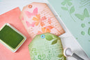 Decorative tags with floral designs and a green stamp pad on a white surface.