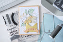 Handmade card with decorative elements on a crafting table with tools and stamps.