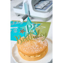 Small round cake with a 'Happy Birthday' topper on a white surface.