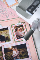 Sizzix machine with photo frames and family photos on a pink surface