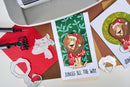 Card with lion illustration and text 'Jungle All The Way' on a crafting table with tools and paper.