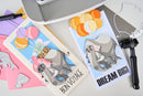 Card with elephant and balloons design, surrounded by crafting tools on a white surface