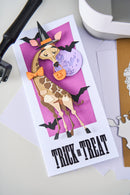 Halloween-themed card with a giraffe wearing a witch hat and holding a pumpkin on a pink background.
