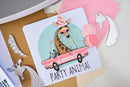 Card with a giraffe in a party hat and sunglasses driving a pink car, surrounded by die-cut shapes on a light background.